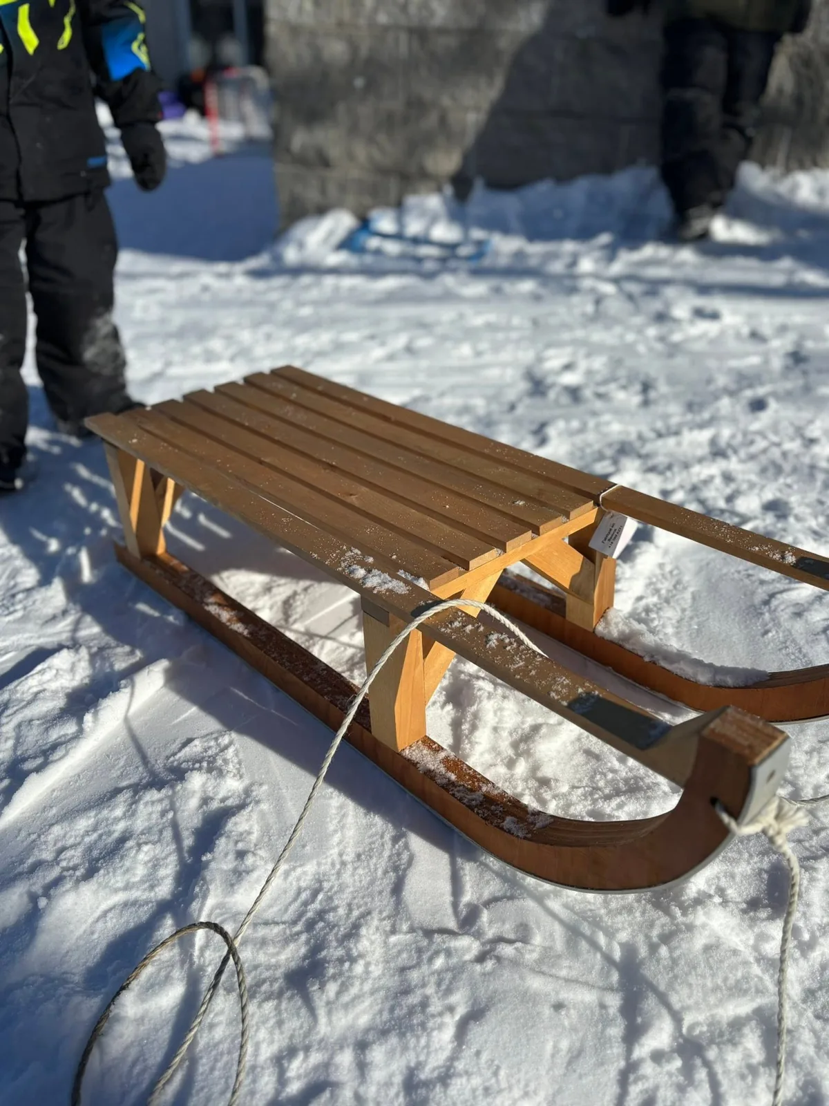 Traîneau de bois posé dans la neige tassée, deux enfants en habit de neige à l’arrière-plan.