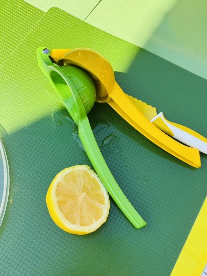 Presse-agrume vert et jaune avec une lime et une moitié de citron sur un tapis de table vert.