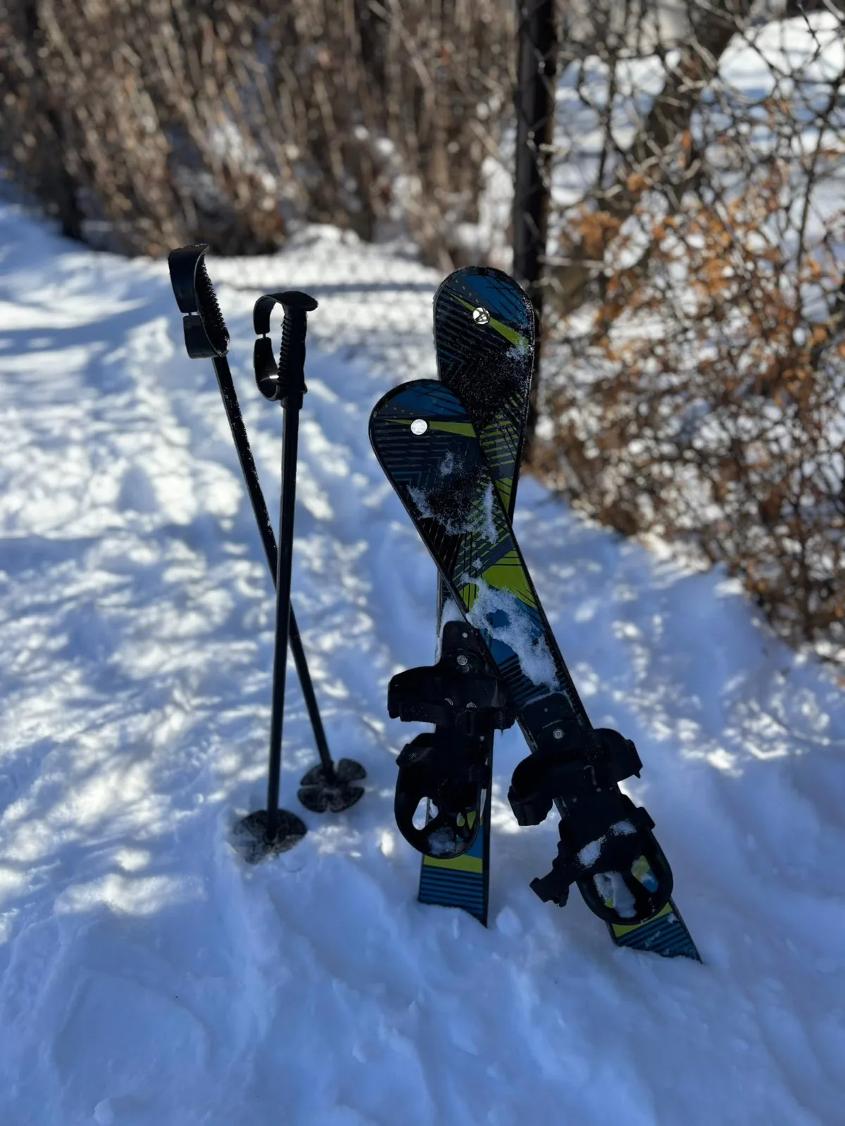 Petits skis et bâtons plantés debout dans la neige, au bord d’un sentier.