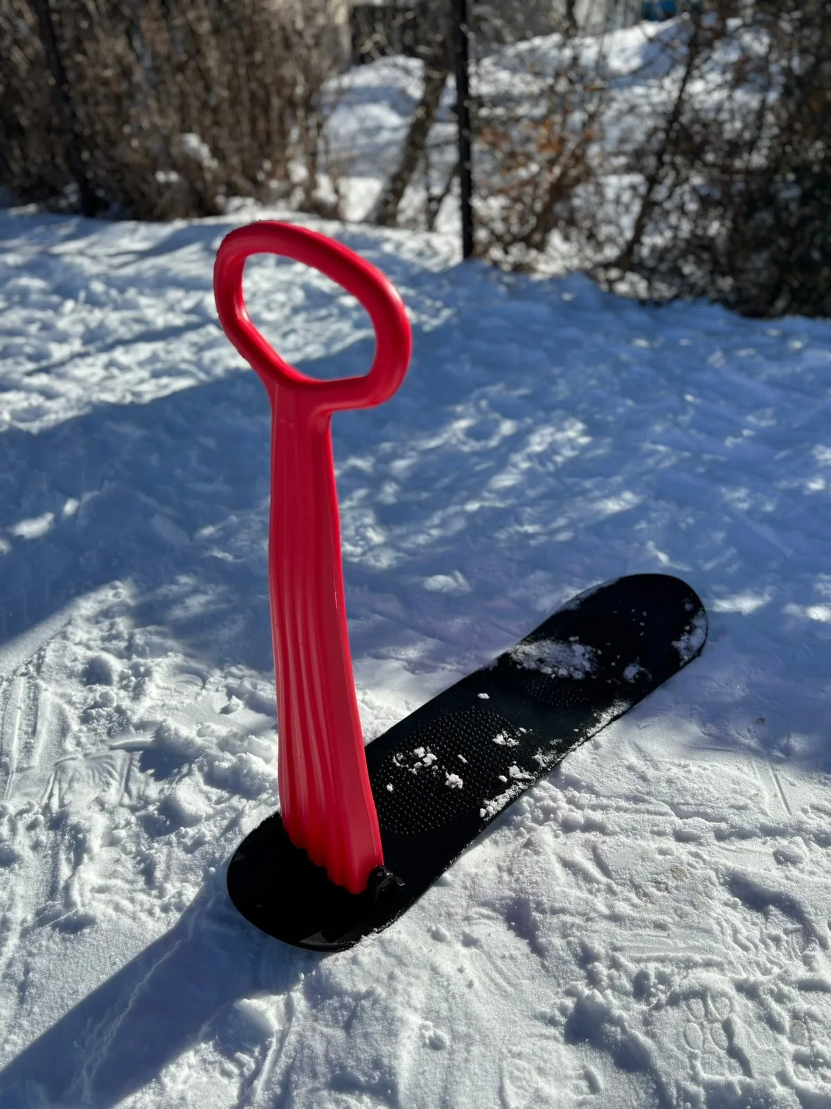 Trottinette des neiges rouge posée sur une planche à glisser noire.
