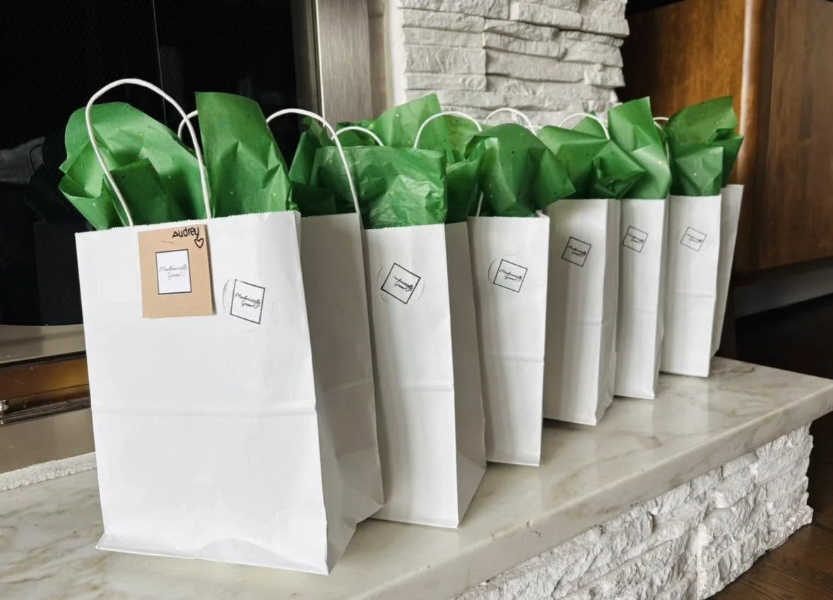 Rangée de petits sacs blancs garnis de papier de soie vert, avec une étiquette au prénom.