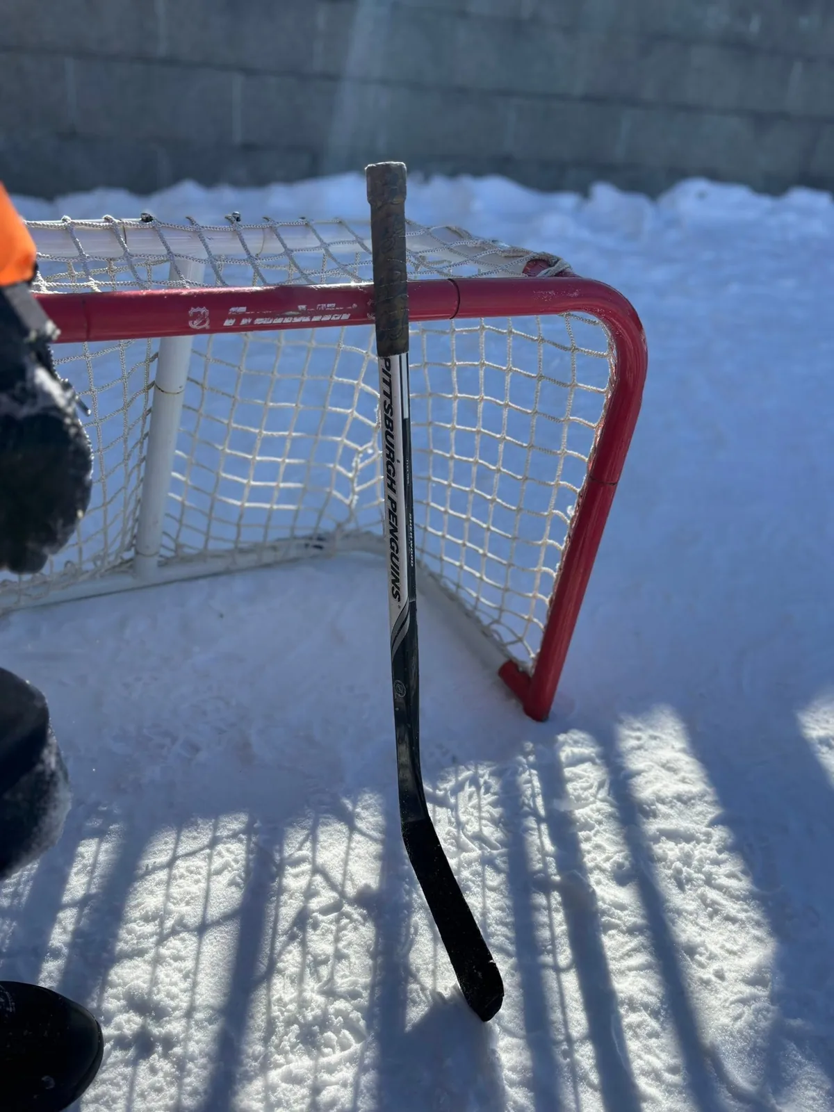 Filet de hockey rouge et bâton plantés dans la neige, par grand soleil.